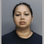 Close-up image of a woman with light brown skin and dark hair, shown in a booking-style photograph with a blank background.