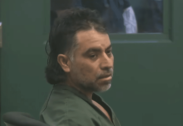 Close-up courtroom photo of a man wearing green clothing in front of a green door.