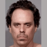 Man with dark curly hair, a mustache and a small goatee faces forward in a tightly cropped portrait.