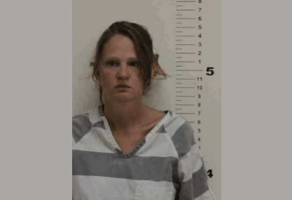 Booking photograph of a woman wearing a striped correctional uniform, posed against a wall-mounted height scale.